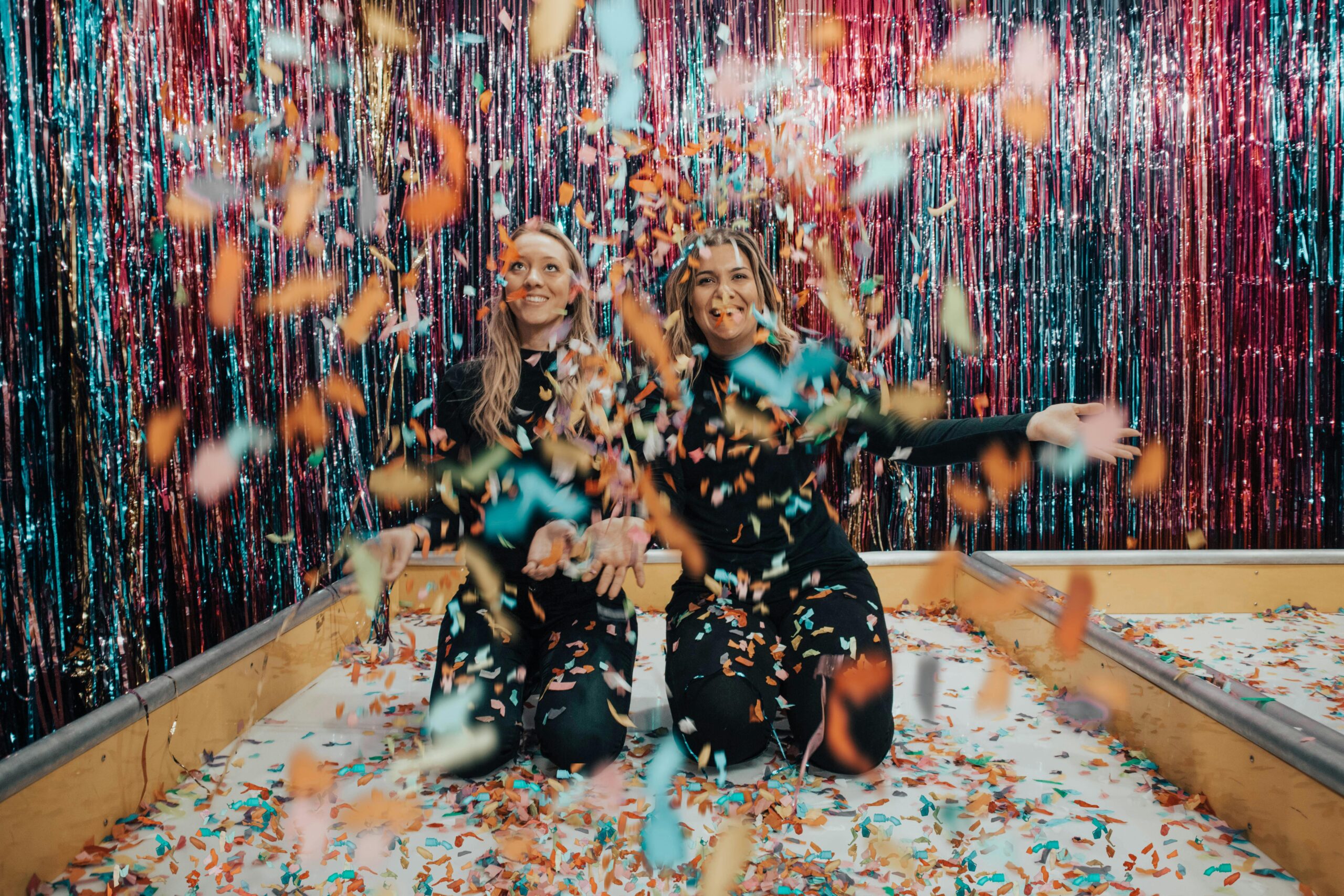 Doua fete care sunt la o petrecere si se distreaza cu confetti